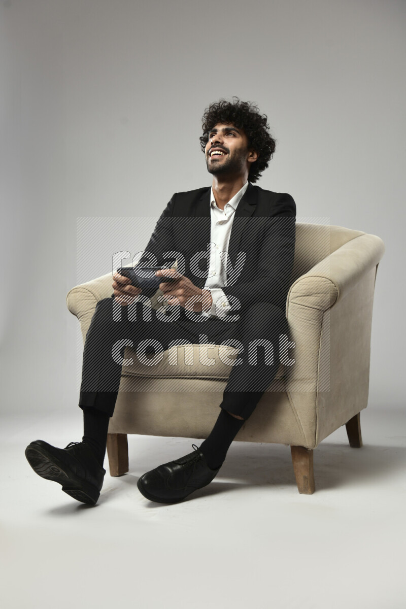 A man wearing formal sitting on a chair gaming on the phone on white background