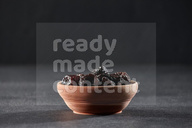 A wooden bowl full of dried plums on a black background in different angles