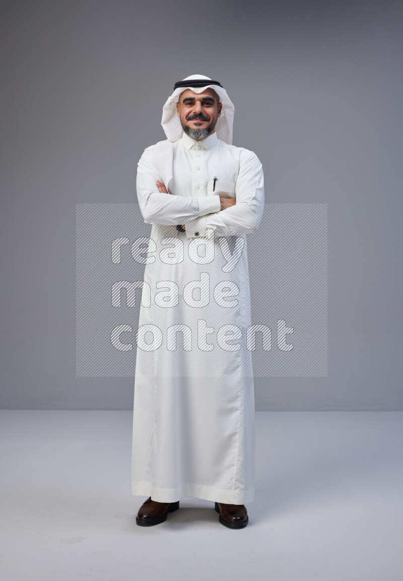 Saudi man Wearing Thob and white Shomag standing with crossed arms on Gray background