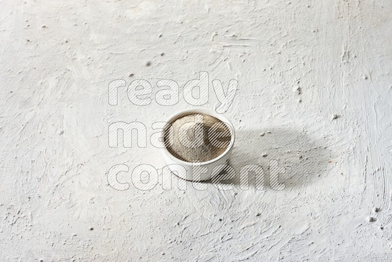 white pottery bowl full of white pepper powder on textured white flooring