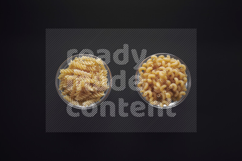 Different pasta types in glass bowls on black background