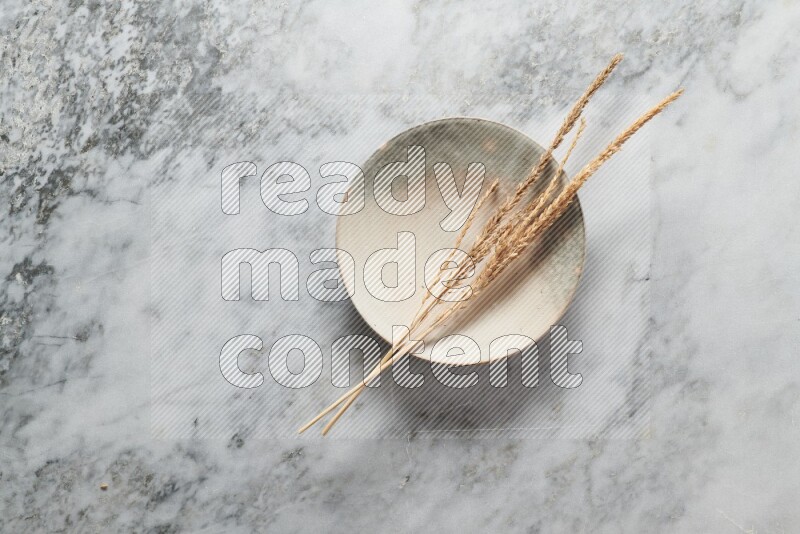 Wheat stalks on multicolored pottery plate on grey marble background