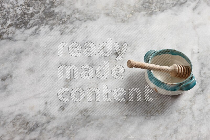Multicolored pottery bowl with wooden honey dipper in it on grey marble background