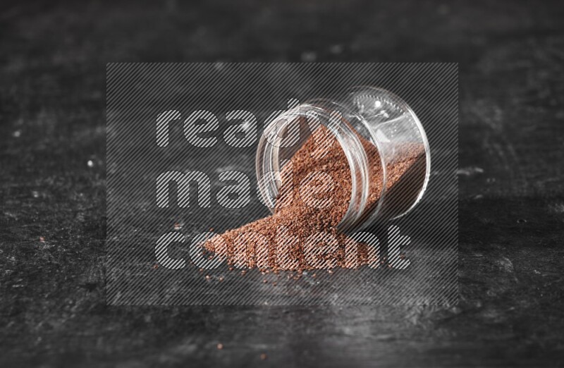A glass jar full of garden cress seeds flipped and seeds spread out on a textured black flooring