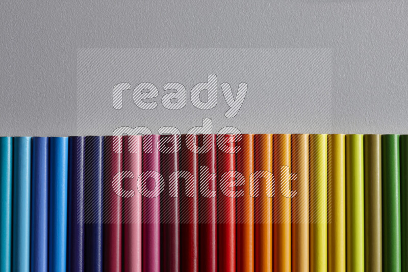 مجموعة من أقلام الرصاص الملونة مرتبة لتعرض تدرجا من الألوان المختلفة علي خلفية رمادية