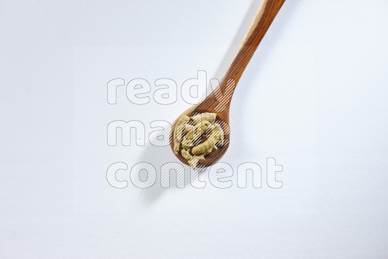 A wooden ladle full of dried turmeric fingers on white flooring