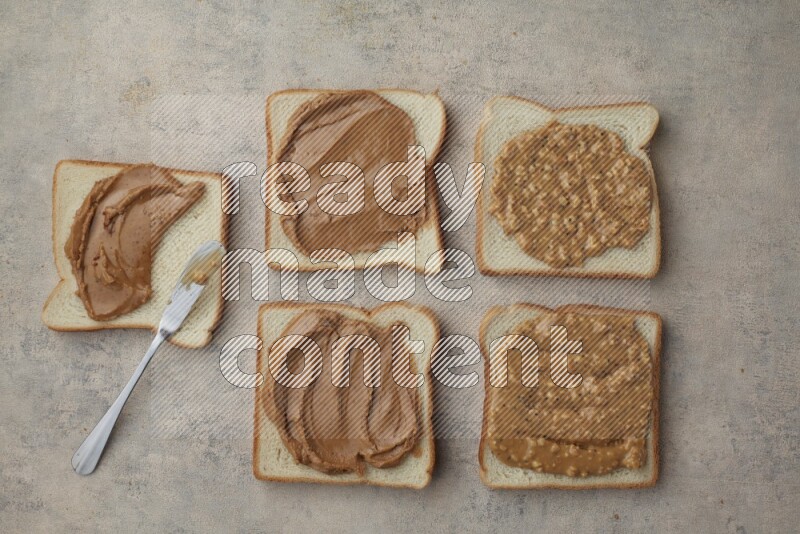 Creamy and Crunchy peanut butter on a white toast with a spreading knife on a light blue textured background