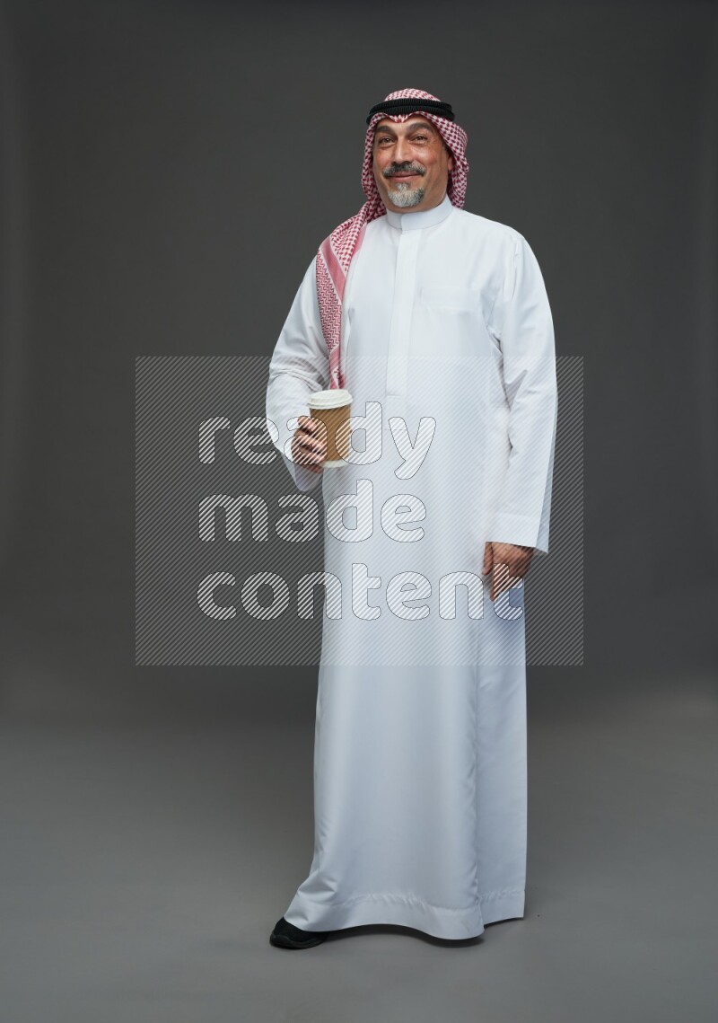 Saudi man with shomag Standing holding paper cup on gray background
