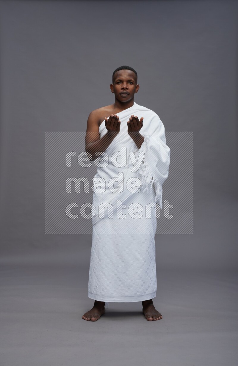A man wearing Ehram Standing dua'a on gray background