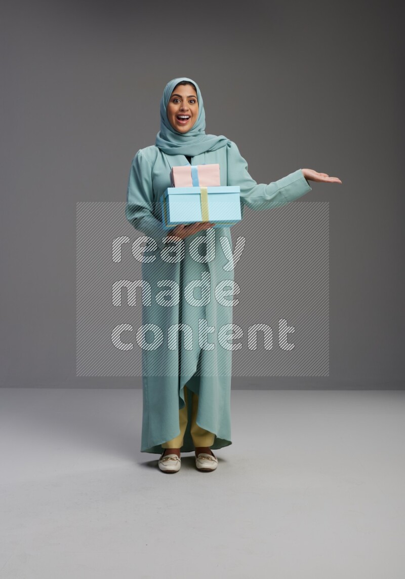Saudi Woman wearing Abaya standing holding gift box on Gray background