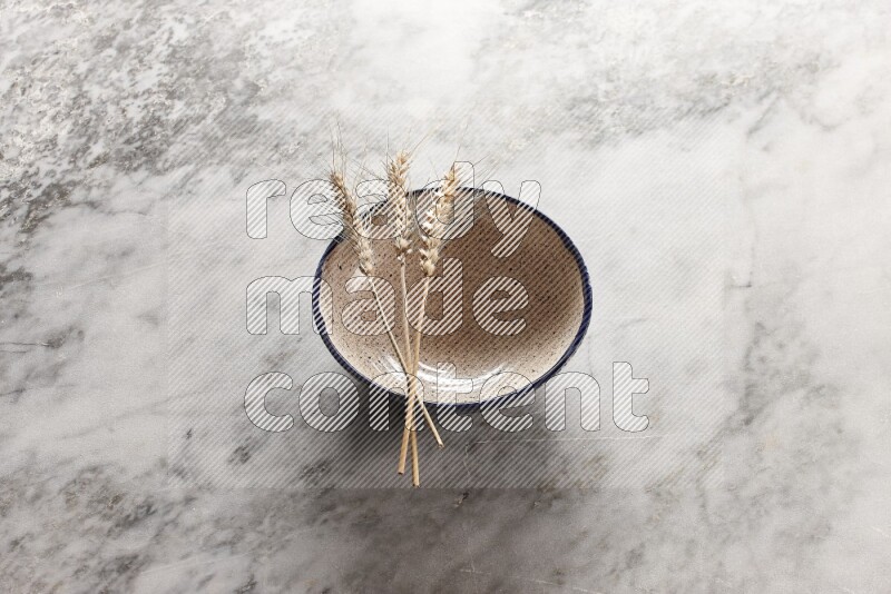 Wheat stalks on multicolored pottery bowl on grey marble background