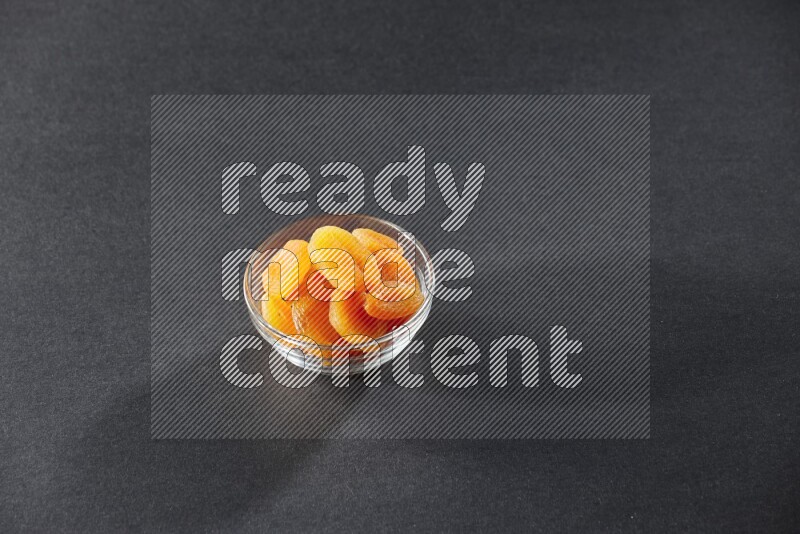 A glass bowl full of dried apricots on a black background in different angles