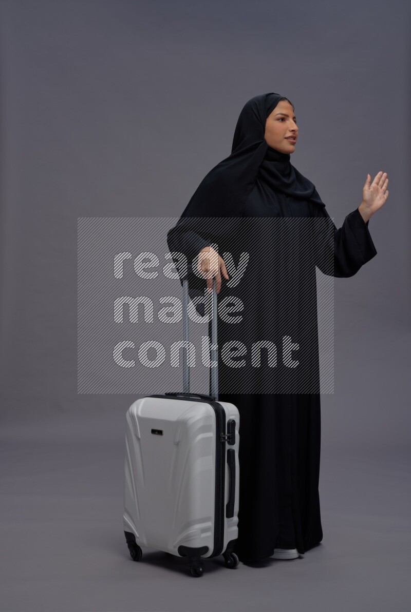 Saudi woman wearing Abaya standing holding bag on gray background
