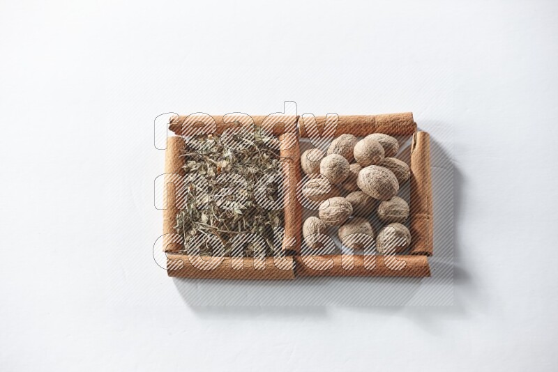 مربعان من أعواد القرفة ممتلئان بالريحان المجفف وجوزة الطيب علي خلفية بيضاء