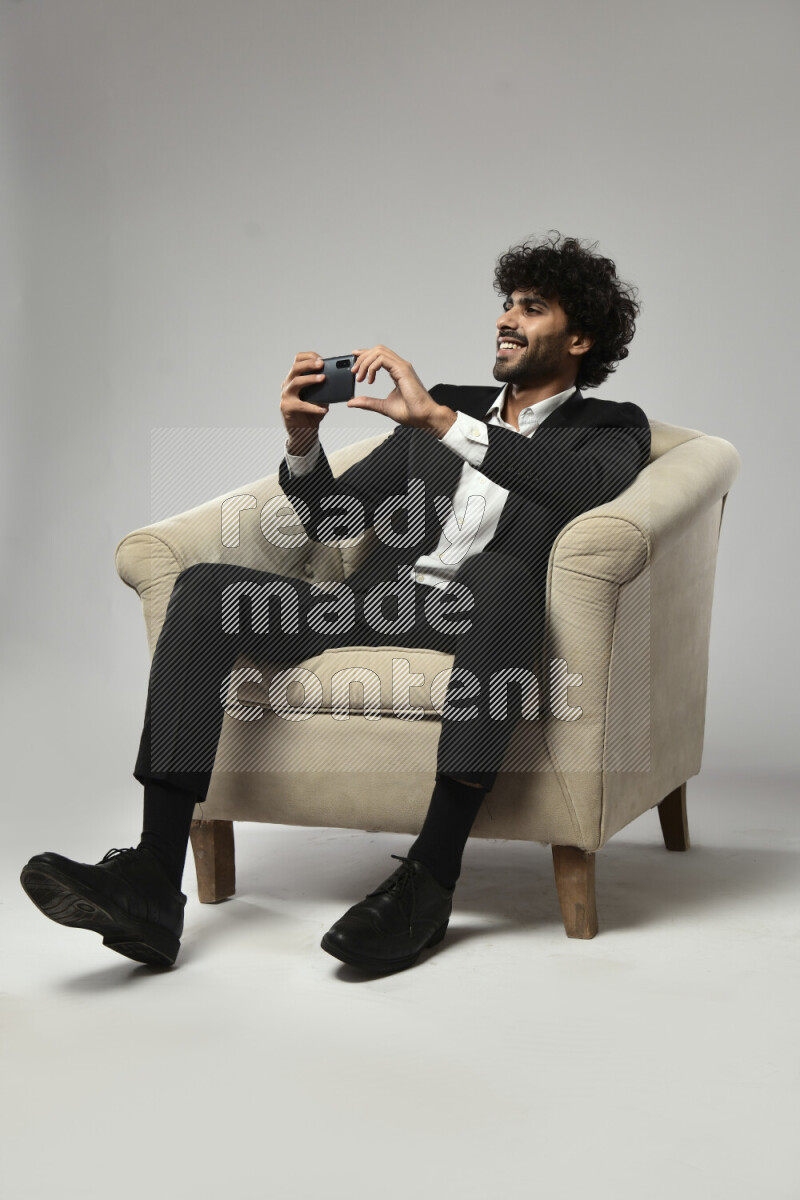 A man wearing formal sitting on a chair shooting with his phone on white background