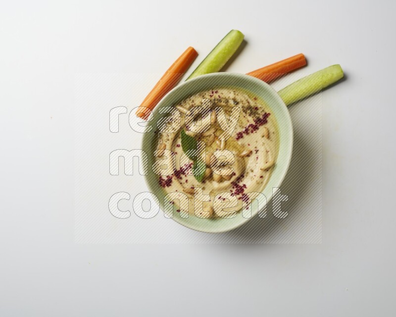 Hummus in a green plate garnished with zattar & sumak on a white background