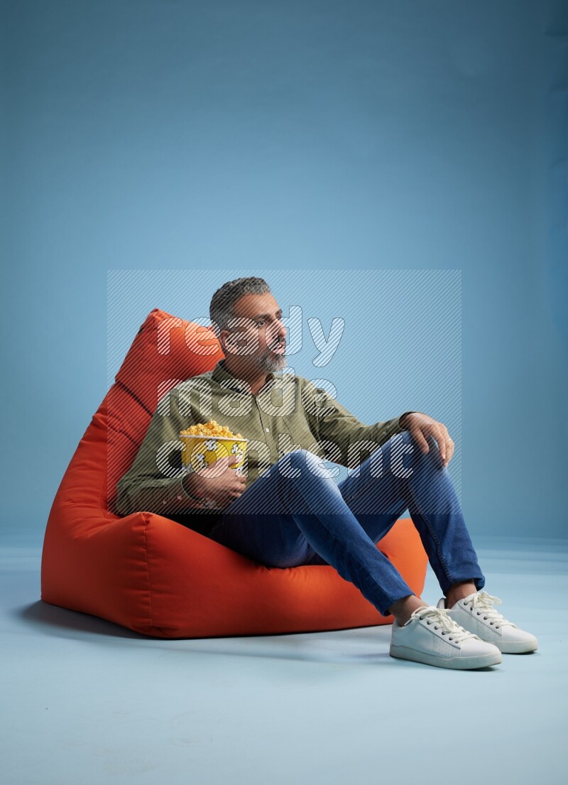 A man sitting on an orange beanbag and eating popcorn