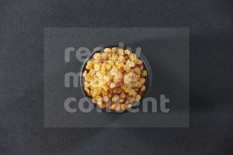 A black pottery bowl full of raisins on a black background in different angles