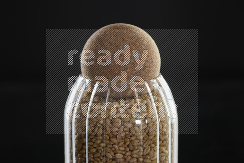 Hulled wheat in a glass jar on black background