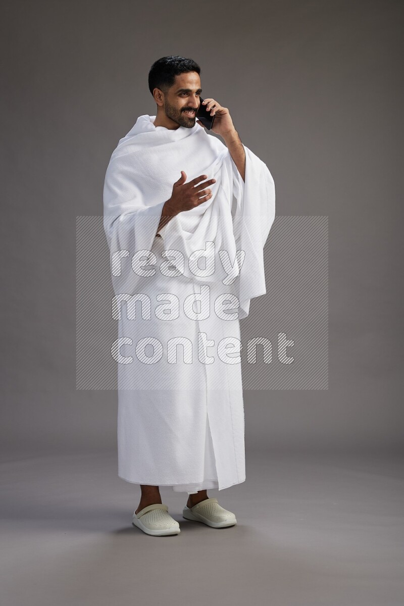 A man wearing Ehram Standing talking on phone on gray background