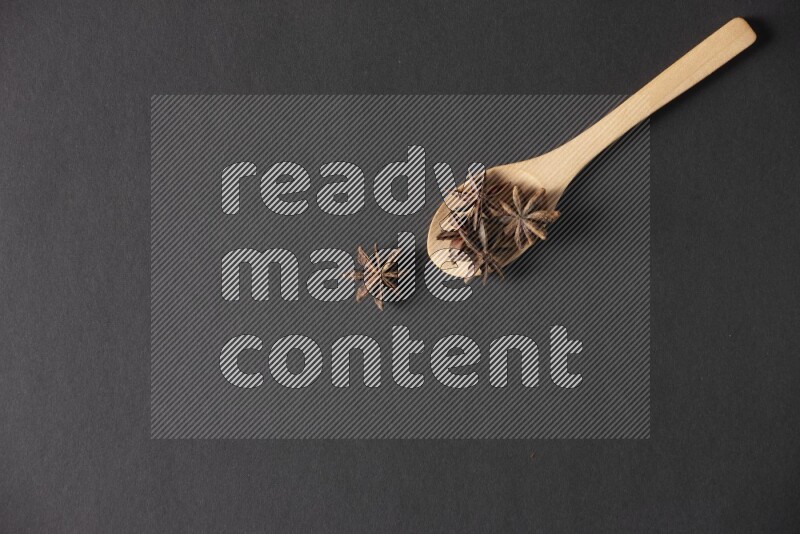 Star Anise in a wooden spoon on more stars anise filling the frame on black flooring