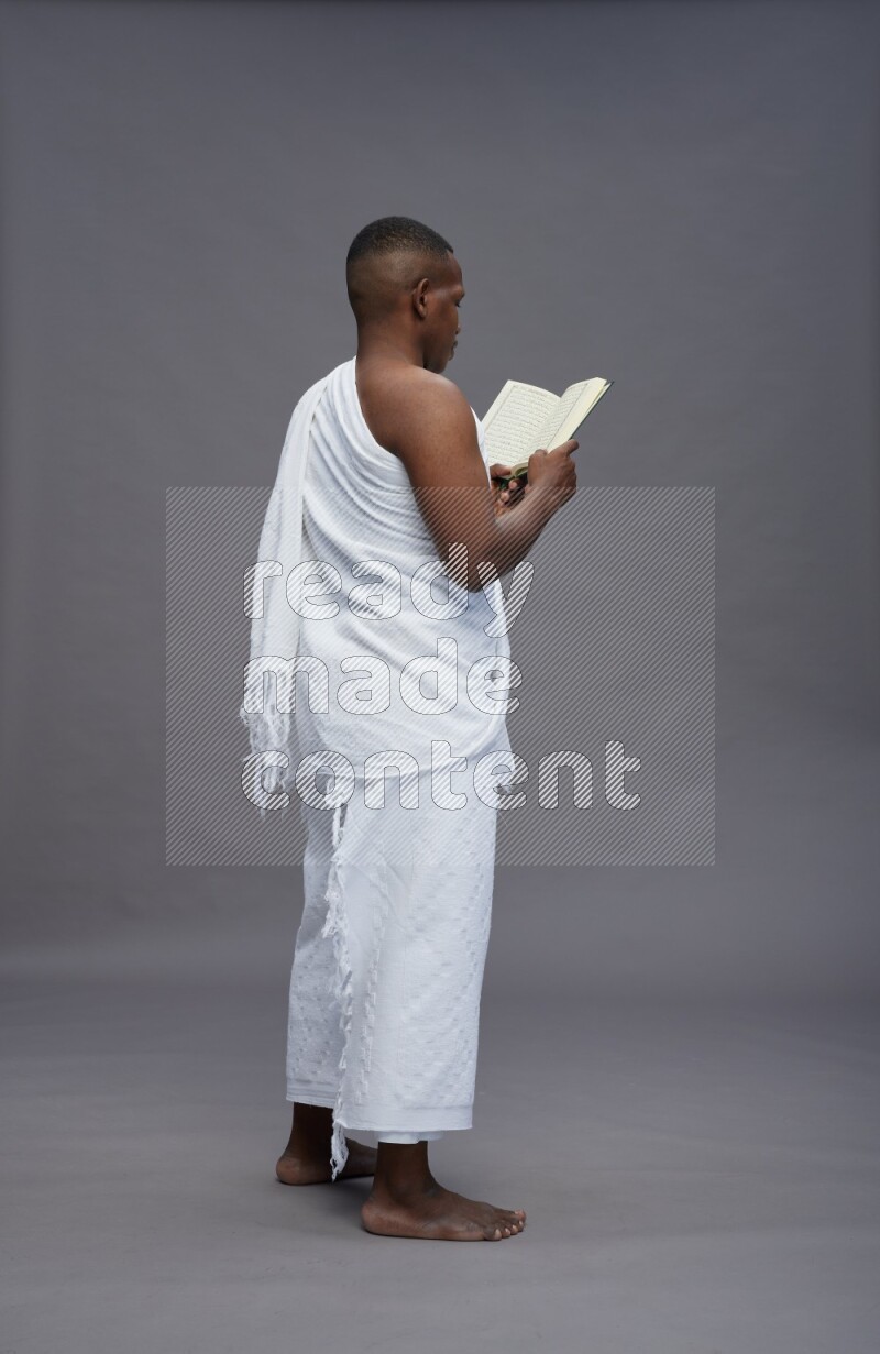 A man wearing Ehram Standing reading quran on gray background