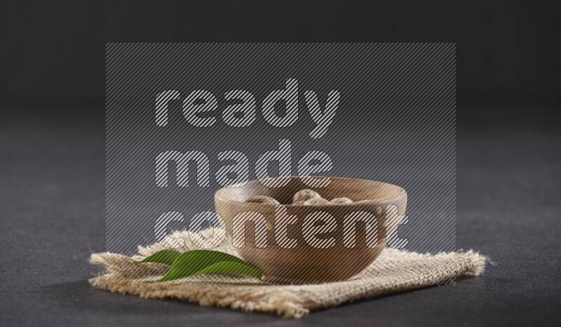 A wooden bowl full of whole nutmeg seeds on burlap fabric on a black flooring