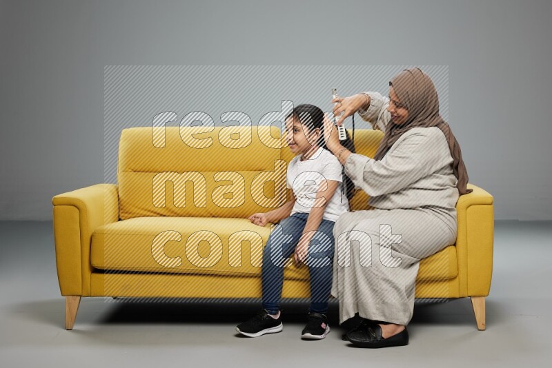 A mother sitting styling hair for her daughter on gray background