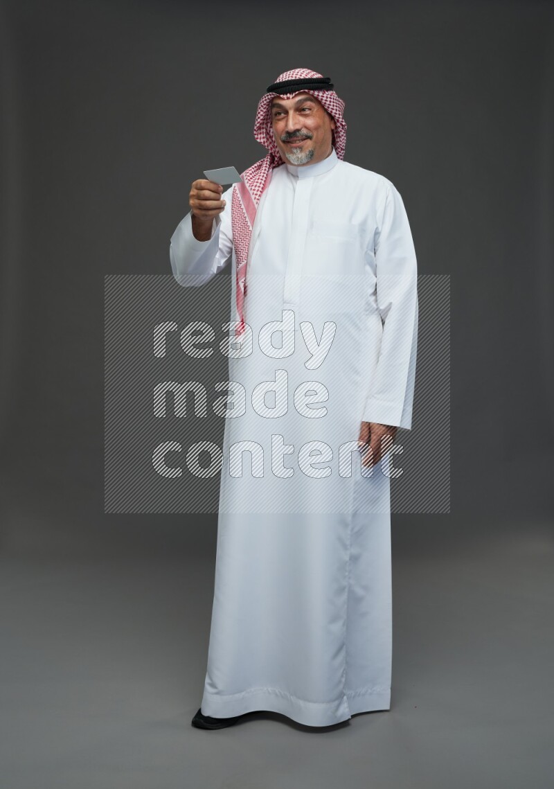 Saudi man with shomag Standing holding ATM card on gray background