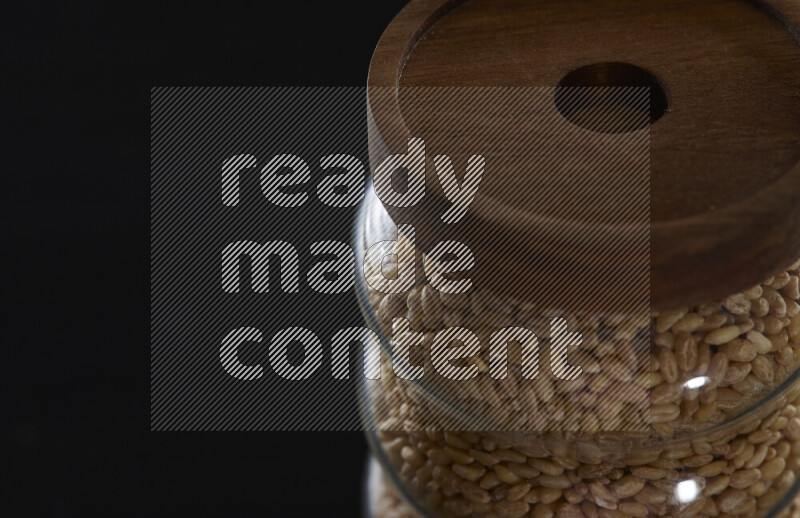 Hulled wheat in a glass jar on black background