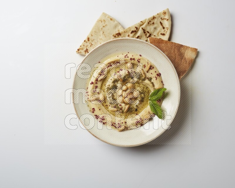 Hummus in a pottry plate garnished with zaatr & sumak on a white background