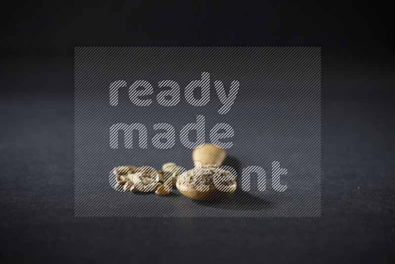 ملعقة خشبية ممتلئة ببودرة الهيل وحبوب الهيل بجانبها على خلفية سوداء