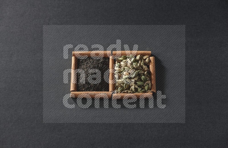 مربعان من أعواد القرفة ممتلئان بحبوب الهيل والشاي الأسود علي خلفية سوداء