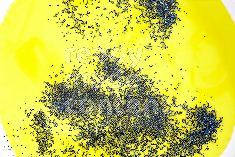 A close-up of sparkling blue glitter scattered on swirling yellow background