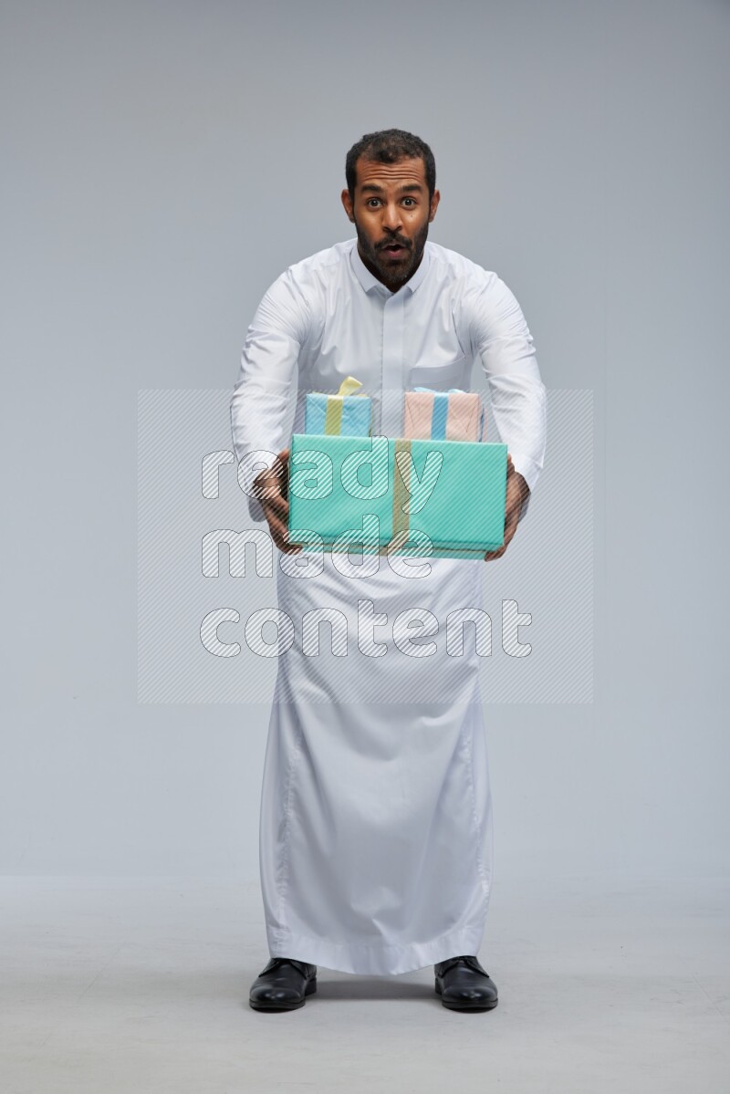 Saudi man Wearing thob standing holding gift box on Gray background