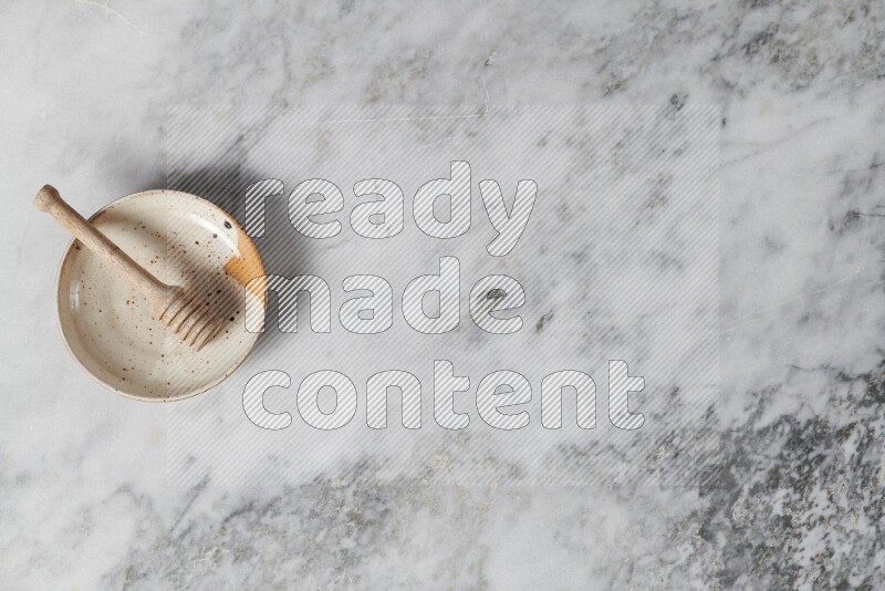 Multicolored pottery plate with wooden honey dipper in it on grey marble background