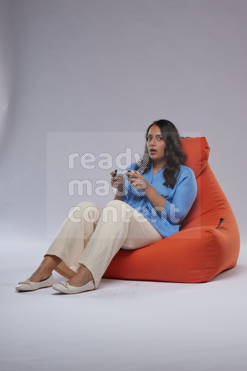 A woman sitting on an orange beanbag and gaming with joystick