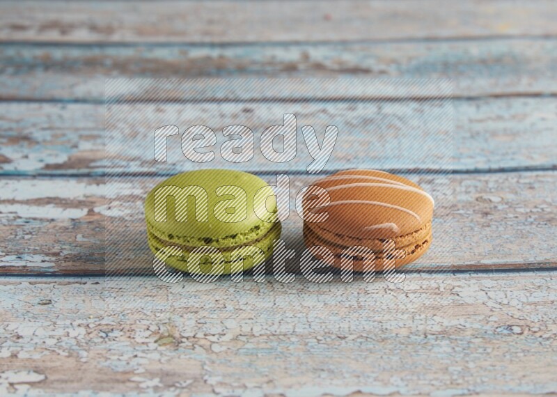 45º Shot of of two assorted Brown Irish Cream, and Green Pistachio macarons  on light blue background