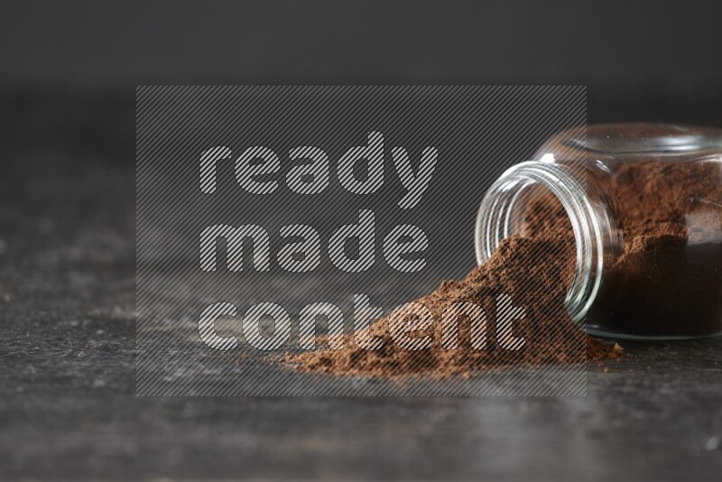 وعاء زجاجي للتوابل مقلوب ممتلئ ببودرة القرنفل والبودرة سقطت منه على أرضية سوداء