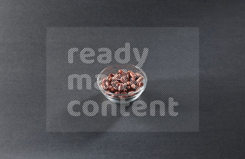 A glass bowl full of red skin peanuts on a black background in different angles