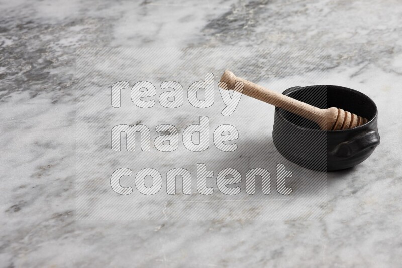 Black pottery bowl with wooden honey dipper in it on grey marble background