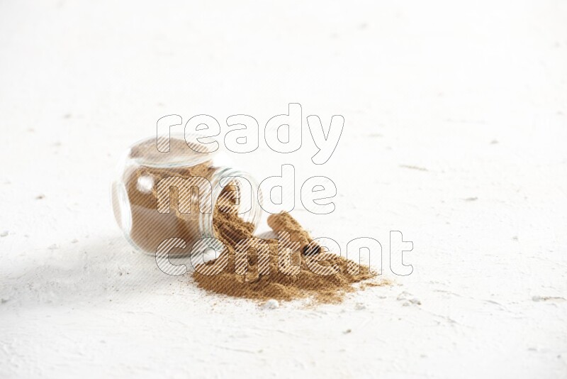 Flipped glass jar full of cinnamon powder with some pieces of cinnamon sticks on a textured white background