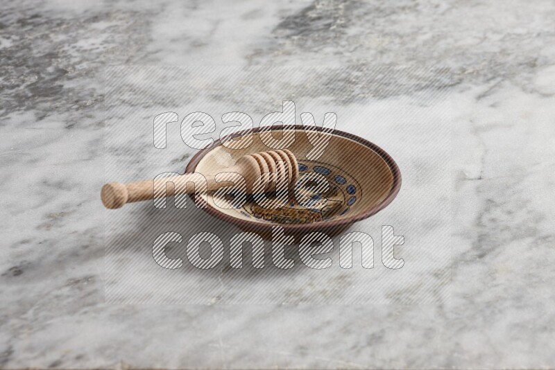 Decorative pottery plate with wooden honey dipper in it on grey marble background