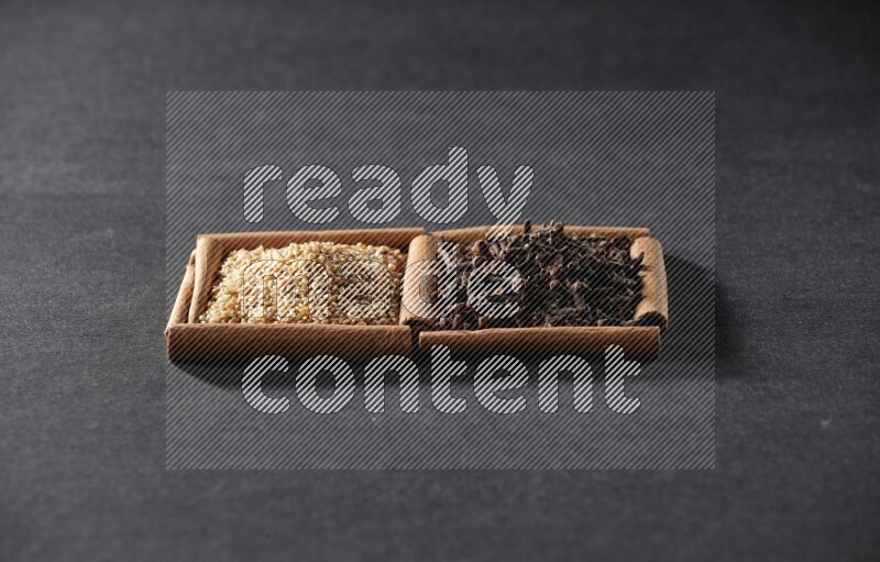 مربعان من أعواد القرفة ممتلئان ببذور السمسم والقرنفل علي خلفية سوداء