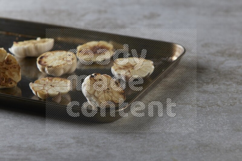 half's roasted garlic in a stainless tray on a grey textured countertop