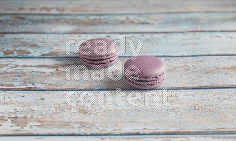45º Shot of two Purple Blueberry macarons on light blue wooden background