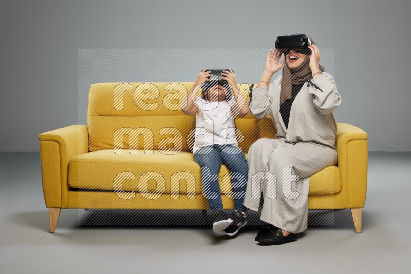 A girl and her mother sitting playing with VR on gray background