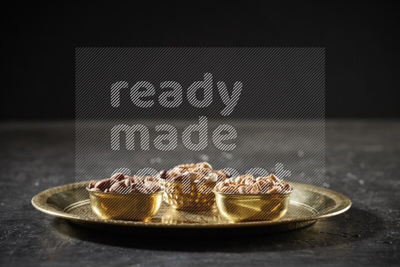 مكسرات في أطباق معدنية على صينية علي خلفية سوداء