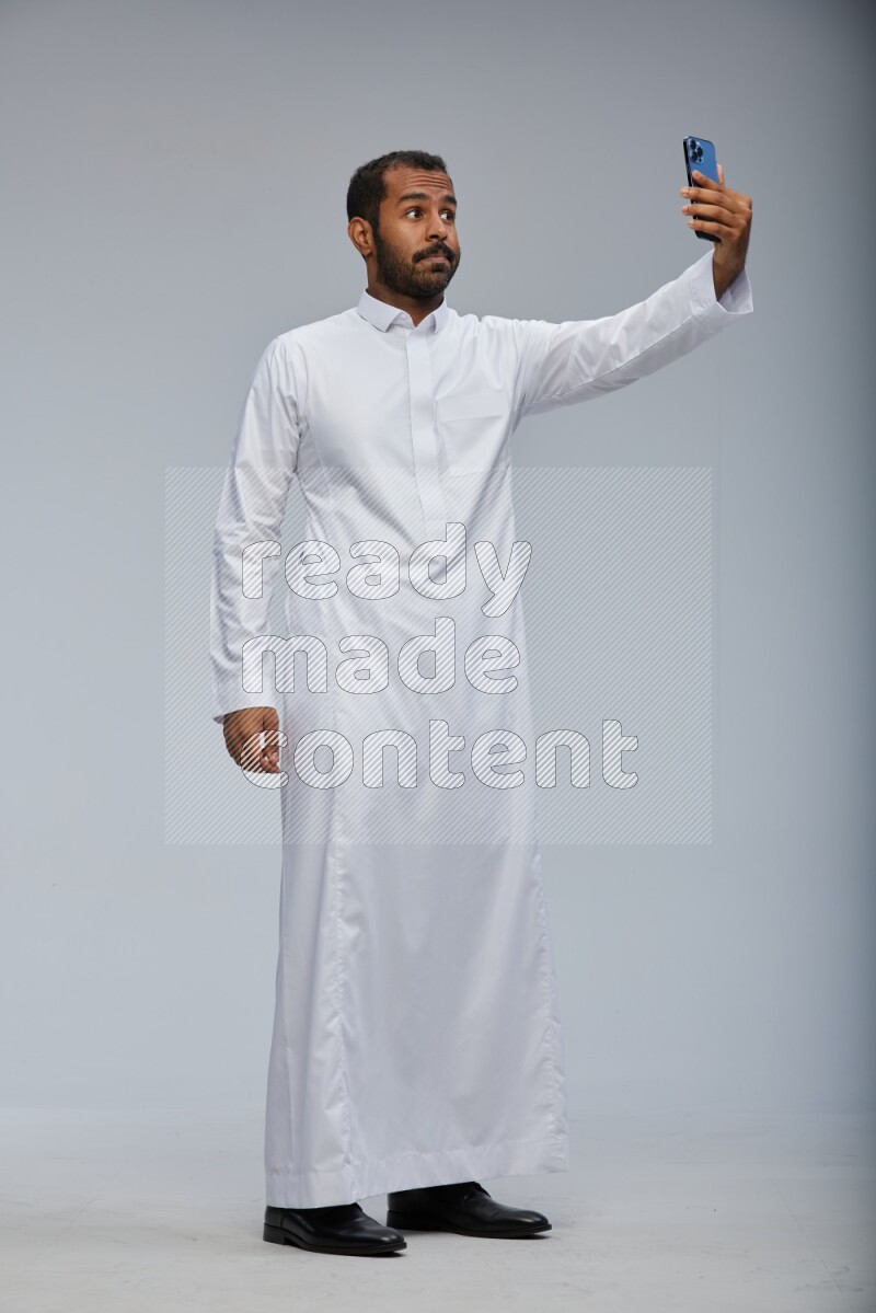 Saudi man wearing Thob standing taking selfie on Gray background