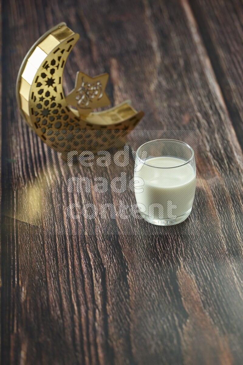 A wooden golden crescent lantern with different drinks, dates, nuts, prayer beads and quran on brown wooden background